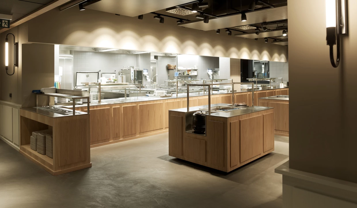 Modern restaurant kitchen with wooden furniture and stainless steel surfaces.