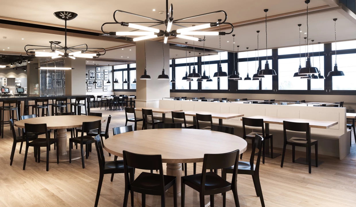 Modern restaurant with round wooden tables and black chairs.