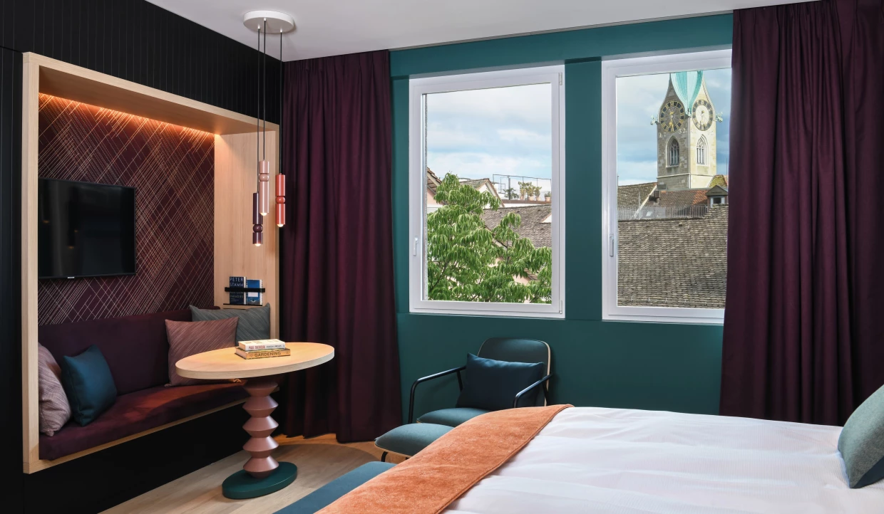 Hotelzimmer in petrol und bordeaux mit Sitznische und Ausblick auf die Kirche St Peter in Zürich