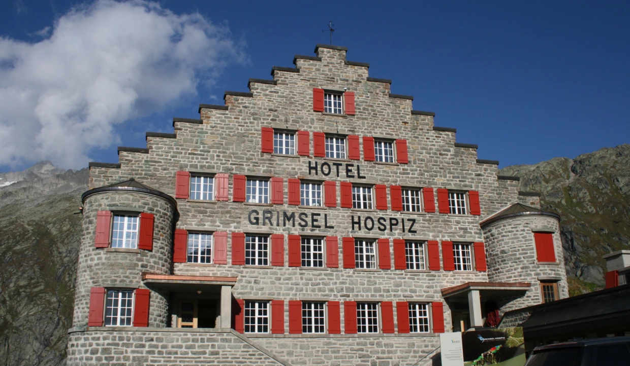 Steingebäude mit roten Fensterläden und Schriftzug Grimsel Hospiz