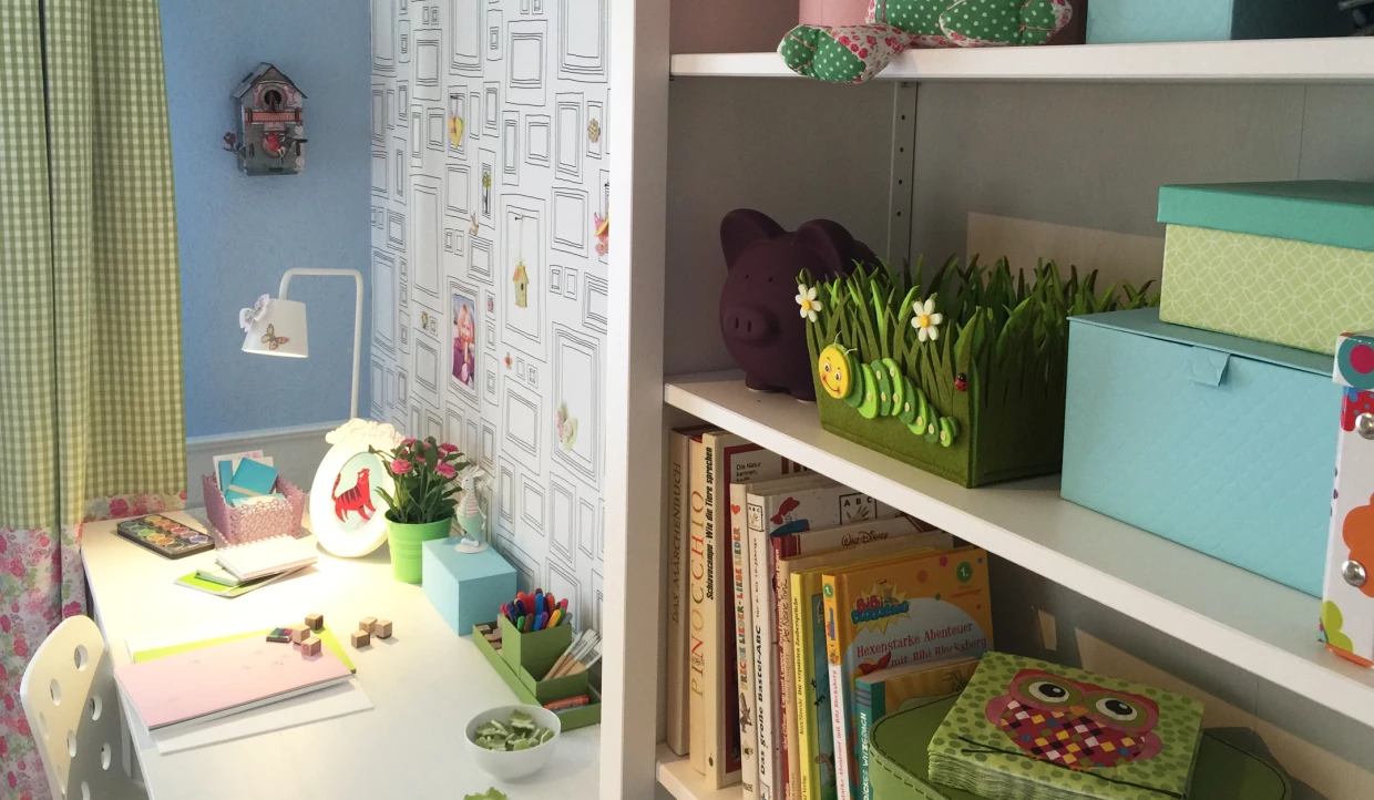 Bürotisch mit Büchern und Deko, eine Lampe und grüne Vorhänge