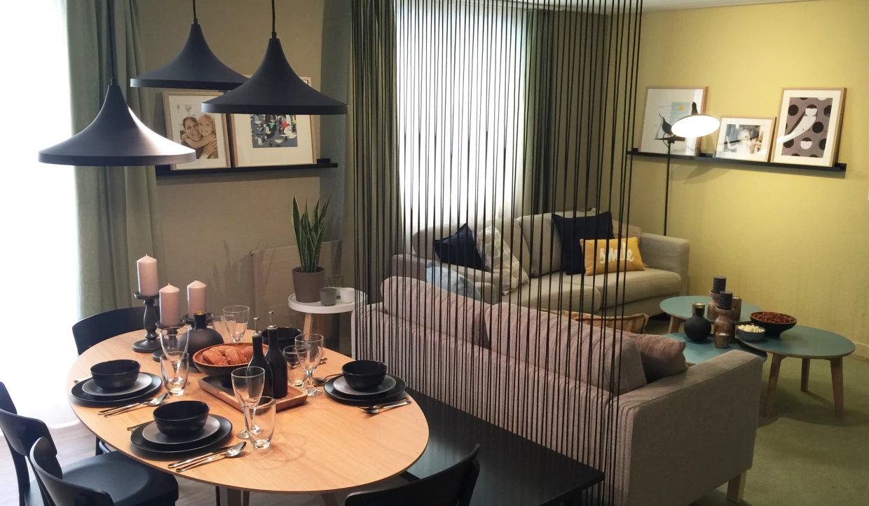 Esszimmer mit Holztisch, schwarzen Tellern und Hängelampen, Wohnzimmer im Hintergrund
