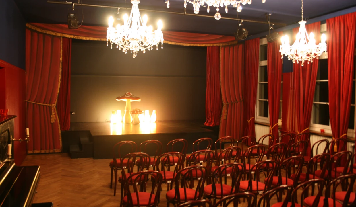 Kleiner Theatersaal mit rotem Vorhang und Kronleuchtern