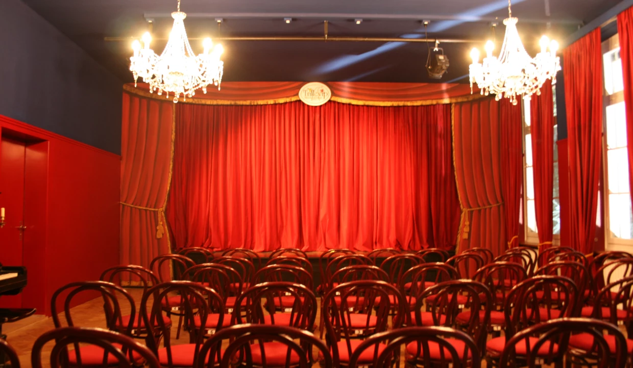 Theatersaal mit Stuhlreihen und geschlossener roter Bühne