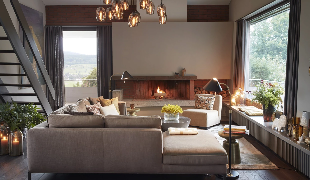 Wohnzimmer mit Sofa, Kamin und Pendelleuchten, große Fenster