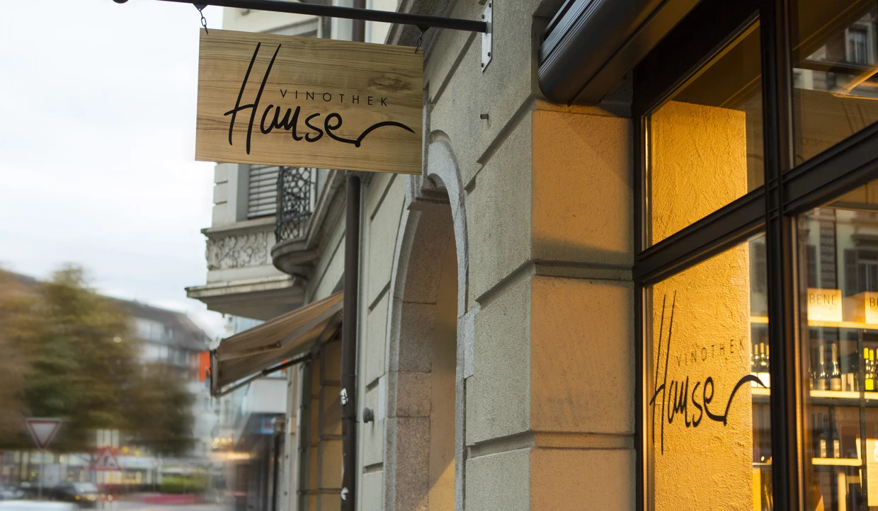 Holzschild mit Schriftzug an Hausfassade bei Dämmerung