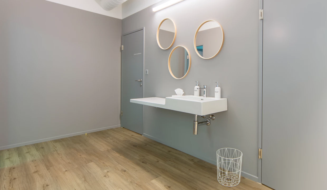 Waschbecken mit drei runden Spiegeln an grauer Wand